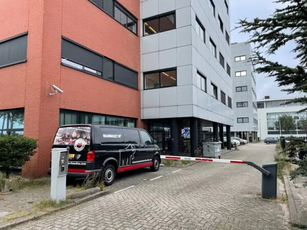 Een zwarte bestelbus van Mammoet staat geparkeerd naast een slagboom bij een kantoorgebouw aan de Karel Doormanweg.